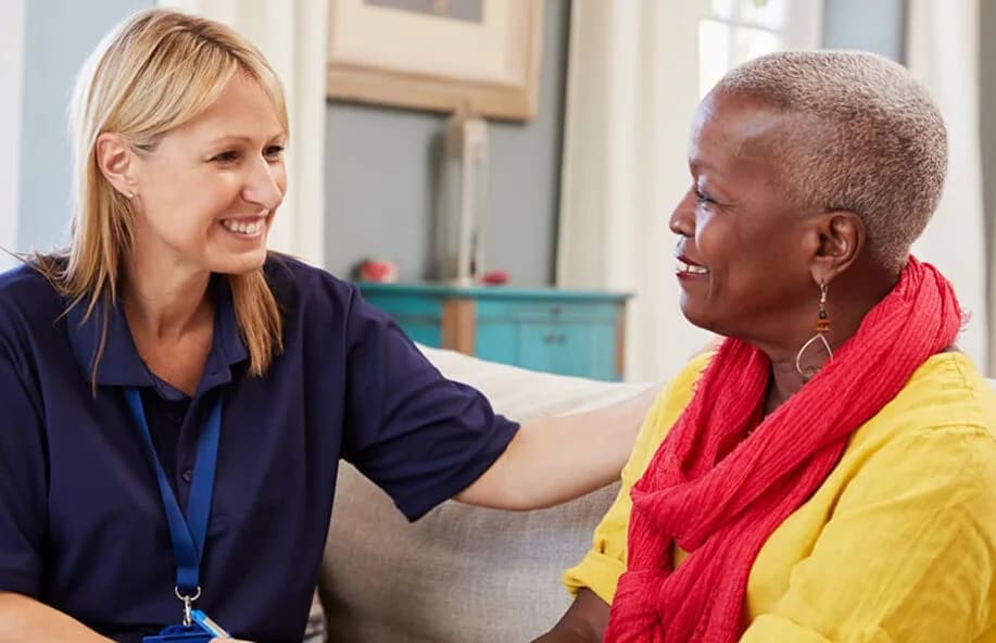 A caregiver sitting with an older woman, both smiling